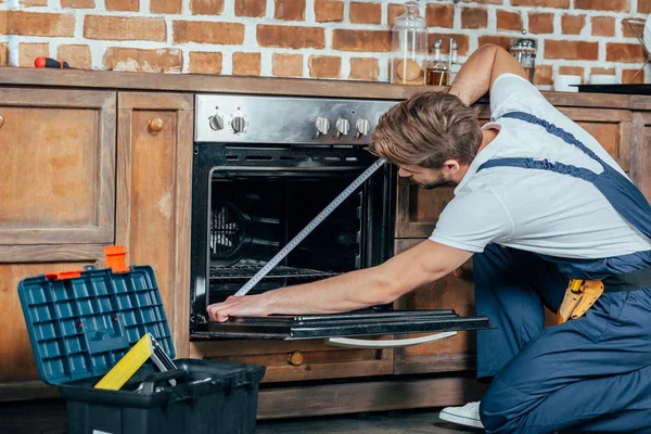 Young foreman in protective workwear measuring oven with tape — Stock Photo