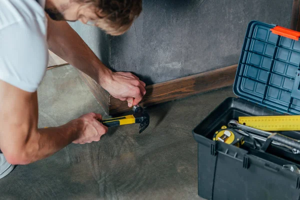 Abgeschnittener Schuss von Handwerker, der Nagel in Fußleiste hämmert — Stockfoto