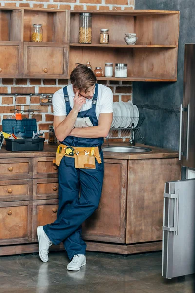 Pensativo joven reparador mirando roto refrigerador en la cocina - foto de stock