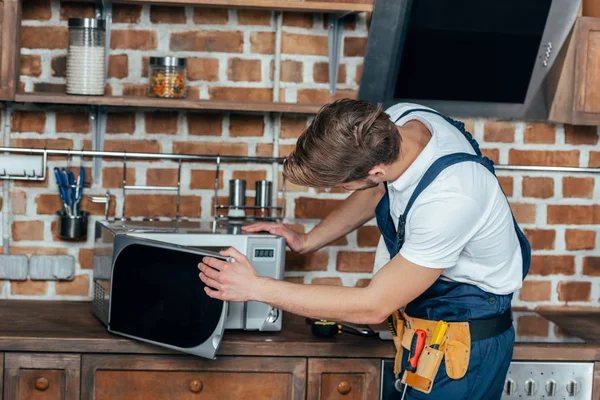 Jovem capataz profissional reparar forno de microondas na cozinha — Fotografia de Stock