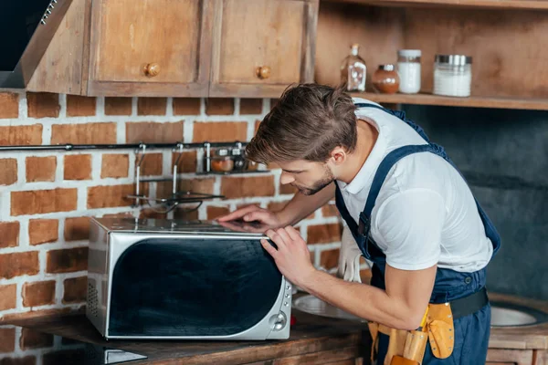 Profesional joven manitas reparación de horno de microondas en la cocina - foto de stock