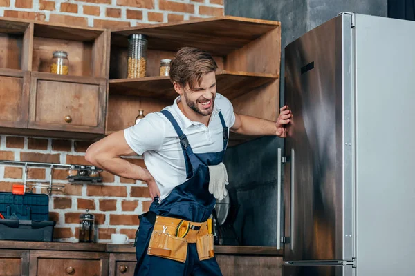 Réparateur souffrant de maux de dos tout en fixant réfrigérateur — Photo de stock