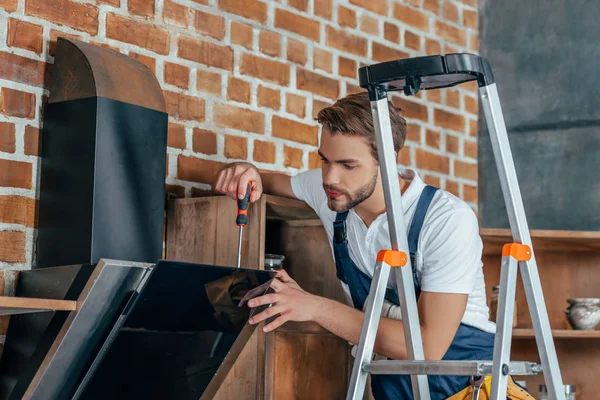 Jeune contremaître debout sur l'échelle et la fixation hotte de cuisine avec tournevis — Photo de stock