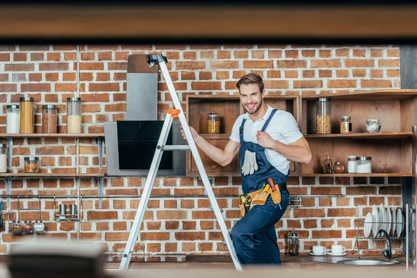 Messa a fuoco selettiva del giovane caposquadra in piedi sulla scala e sorridente alla fotocamera mentre fissa la cappa da cucina — Foto stock