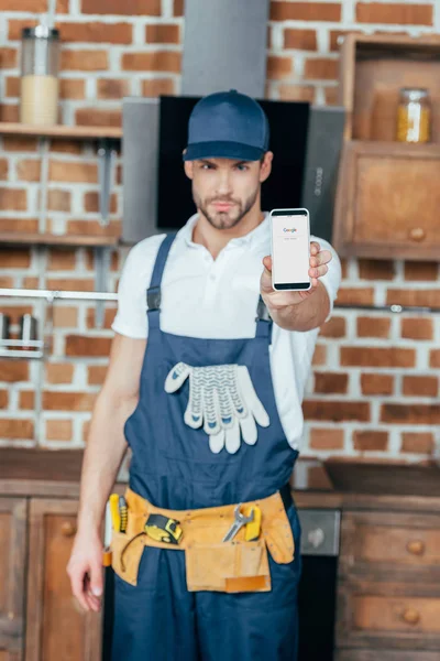 Schöner junger professioneller Hausmeister zeigt Smartphone mit google-Webseite — Stockfoto