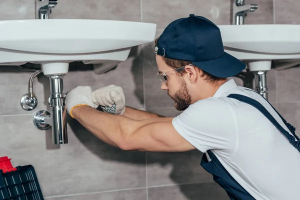 Close-up view of young professional plumber fixing sink in bathroom — Stock Photo