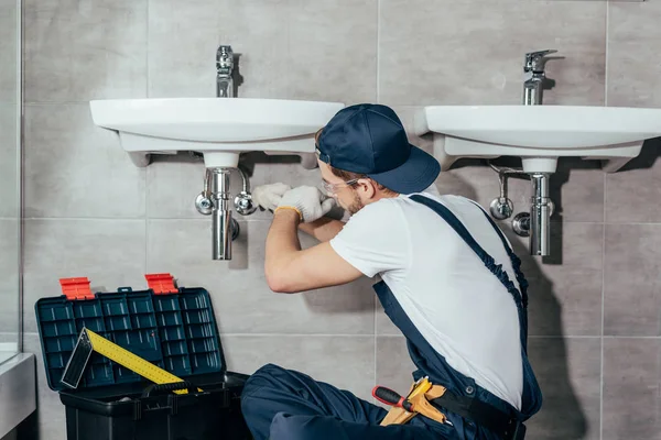 Visão traseira da pia de fixação profissional jovem encanador no banheiro — Fotografia de Stock