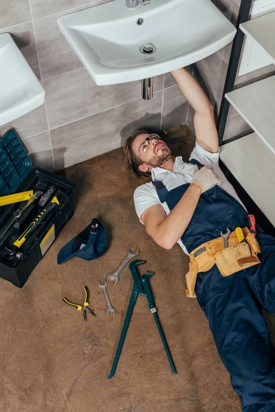 Hochwinkel-Ansicht des jungen männlichen Klempners Befestigung Waschbecken im Badezimmer — Stockfoto