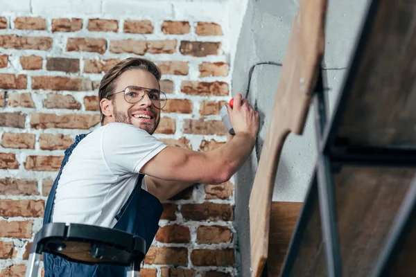 Apuesto joven electricista profesional sonriendo a la cámara - foto de stock