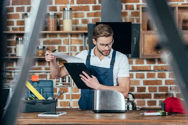 Selective focus of young handyman holding clipboard and fixing toaster — Stock Photo