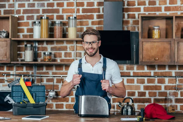 Jeune réparateur avec clé et tournevis souriant à la caméra tout en réparant grille-pain — Photo de stock