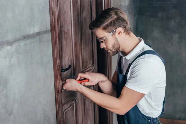 Giovane lavoratore riparazione serratura della porta con cacciavite — Foto stock