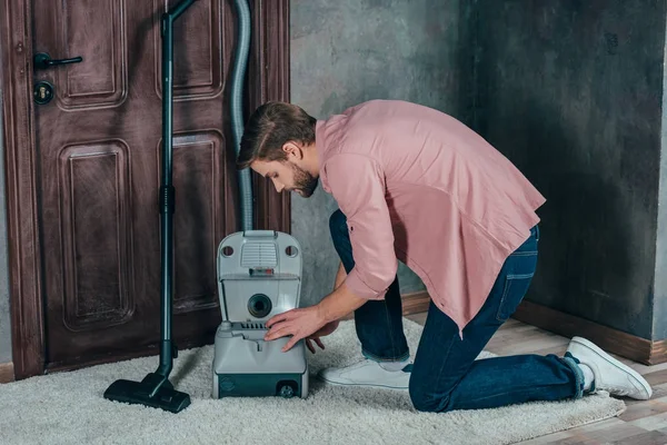 Vue latérale du jeune homme fixant aspirateur cassé à la maison — Photo de stock