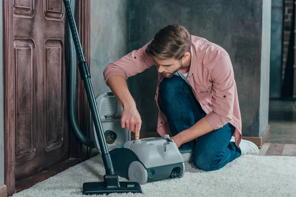 Joven mirando la aspiradora rota y fijándola en casa - foto de stock