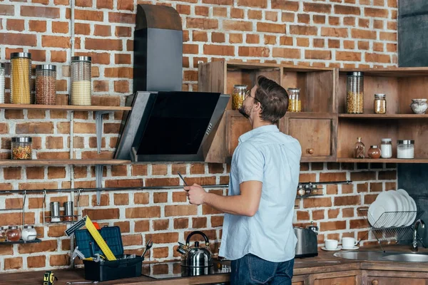 Jovem em óculos segurando chave de fenda e olhando para exaustão na cozinha — Fotografia de Stock