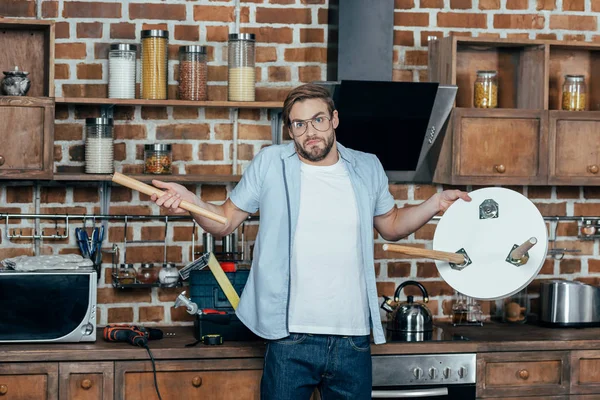 Disappointed young man in eyeglasses holding broken stool and looking at camera — Stock Photo