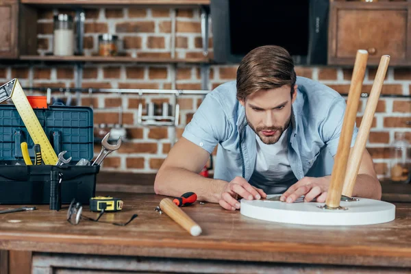 Konzentrierter junger Mann repariert Hocker mit Werkzeug zu Hause — Stockfoto