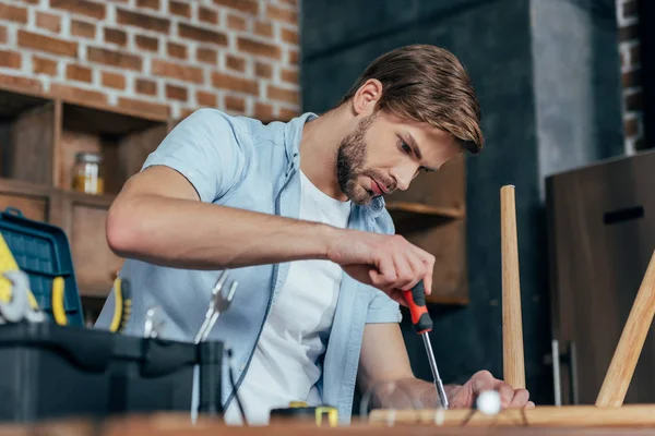 Focused young man repairing stool with screwdriver — Stock Photo