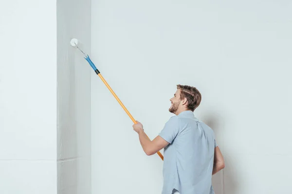 Vista laterale del giovane sorridente che utilizza rullo di vernice mentre dipinge la parete a casa — Foto stock