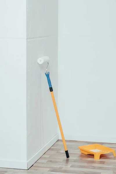 Rolo de pintura e recipiente com tinta branca na sala vazia — Fotografia de Stock