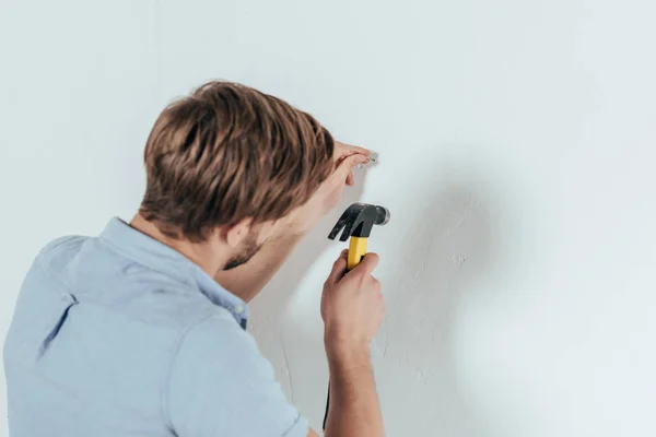 Back view of young man hammering nail in wall at home — Stock Photo