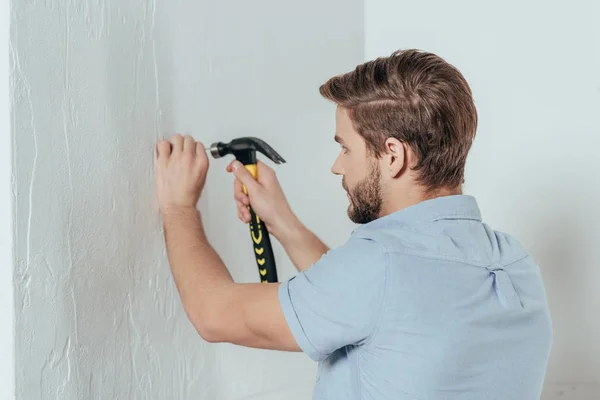 Young man hammering nail in wall at home — Stock Photo