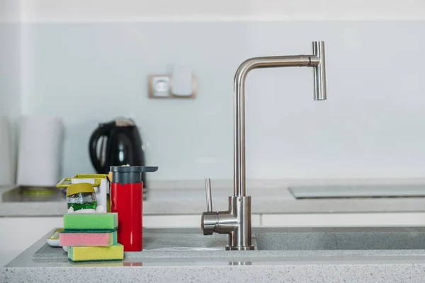 Esponjas lavavajillas cerca del grifo de agua en la cocina - foto de stock