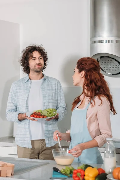 Подружка готовит тесто и парень держит тарелку с овощами — стоковое фото