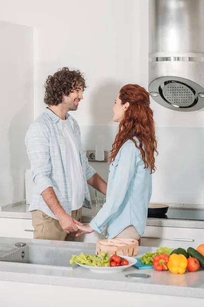 Pareja feliz tomados de la mano y mirándose en la cocina - foto de stock