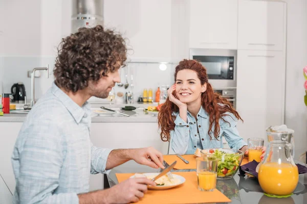 Улыбающаяся девушка смотрит, как парень ест домашнюю еду — стоковое фото