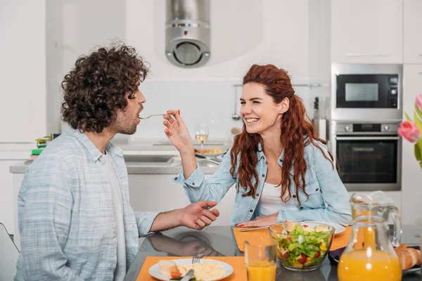 Sourire petite amie nourrir petit ami dans la cuisine — Photo de stock