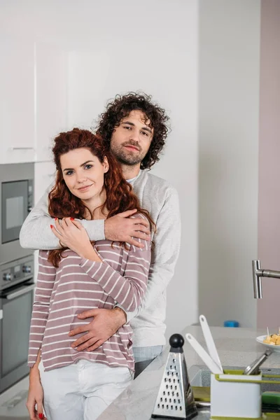 Copain étreignant petite amie à la cuisine et ils regardent caméra — Photo de stock