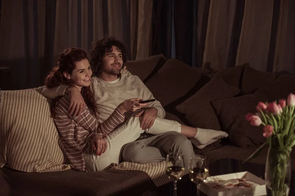 Счастливая пара смотрит телевизор на диване вечером — стоковое фото