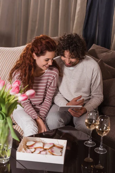 Coppia sorridente utilizzando tablet mentre seduto sul divano a casa — Foto stock