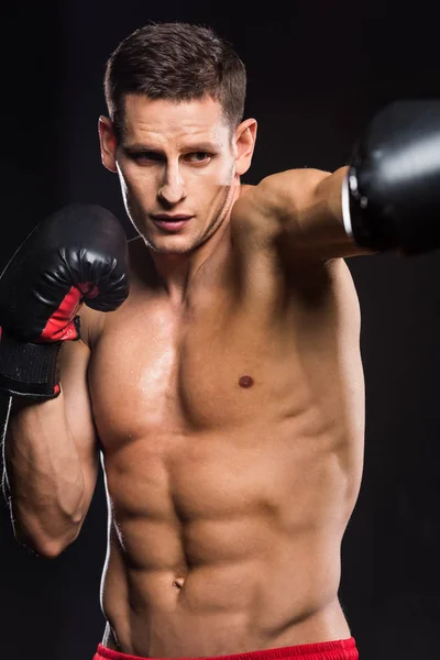 Selective focus of young shirtless sportsman in boxing gloves boxing isolated on black — Stock Photo