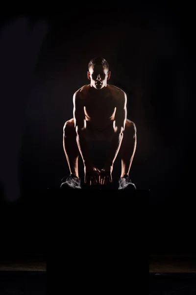 Silhouette of athletic young sportsman jumping from block on black — Stock Photo