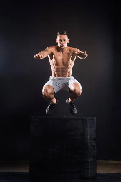 Athletic young sportsman jumping from block on black — Stock Photo