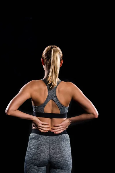 Back view of athletic young woman in sportswear standing with hands on waist isolated on black — Stock Photo