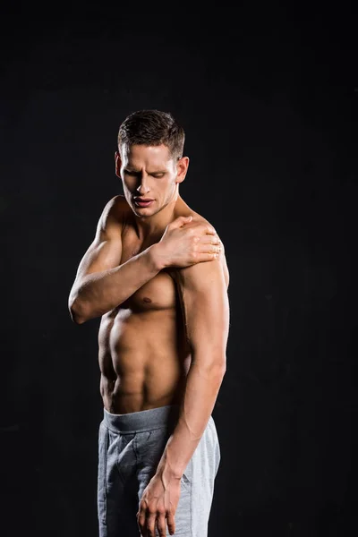 Shirtless muscular sportsman suffering from pain in arm isolated on black — Stock Photo