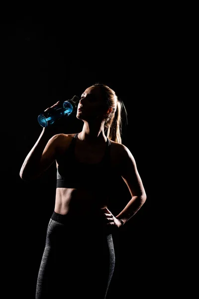 Silhouette of sportswoman drinking water from bottle isolated on black — Stock Photo