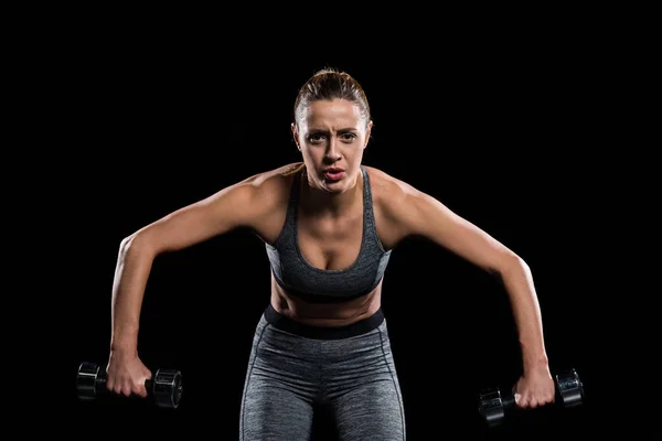 Cansado desportivo jovem mulher exercitando com halteres e olhando para a câmera isolada no preto — Fotografia de Stock
