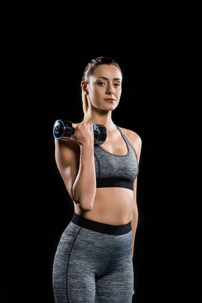 Athletic sportswoman holding dumbbell and looking at camera isolated on black — Stock Photo