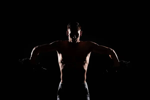 Silhouette of muscular sportsman holding dumbbells isolated on black — Stock Photo