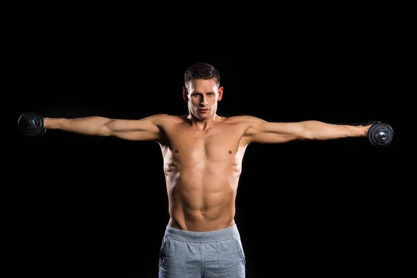 Musculoso deportista sin camisa sosteniendo mancuernas y mirando a la cámara aislada en negro - foto de stock