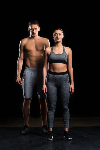 Athletic young couple in sportswear looking at camera on black — Stock Photo
