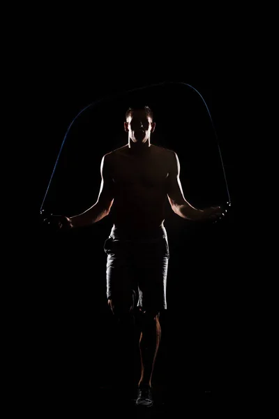 Silhouette of athletic sportsman jumping with skipping rope isolated on black — Stock Photo