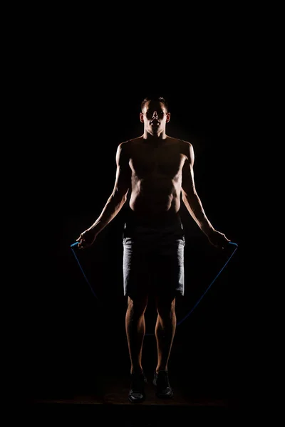 Silhouette of sportsman jumping with skipping rope on black — Stock Photo