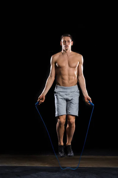 Muscular shirtless sportsman jumping with skipping rope on black — Stock Photo