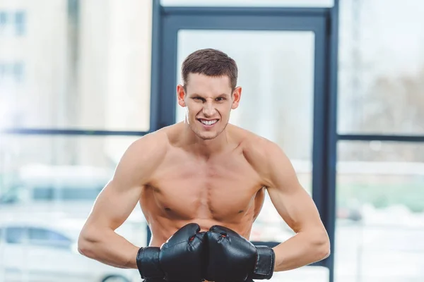 Junger, schulterfreier, muskulöser Boxer mit Boxhandschuhen, der im Fitnessstudio in die Kamera schaut — Stockfoto