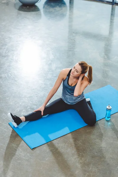 Blick aus der Vogelperspektive auf junge Sportlerin, die auf Yogamatte sitzt und im Fitnessstudio trainiert — Stockfoto